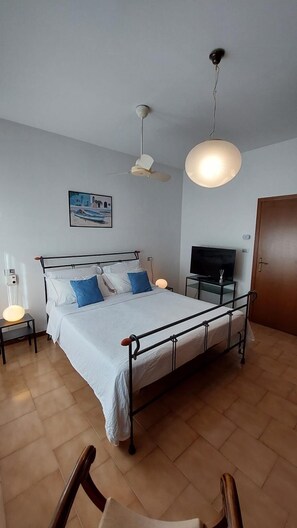 Ein Schlafzimmer mit Bett, Deckenventilator, Fernseher und einer Tür.