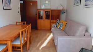 A living room with a sofa, a glass coffee table, a wooden dining table with chairs, a cabinet, and a hanging light fixture. - Casa Pisani - Two Bedroom Apartment, Sleeps 6 (Rimini)
