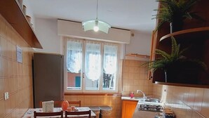 A compact kitchen with a dining area, a window with curtains, a hanging light fixture, and a fire extinguisher. - Casa Pisani - Two Bedroom Apartment, Sleeps 6 (Rimini)