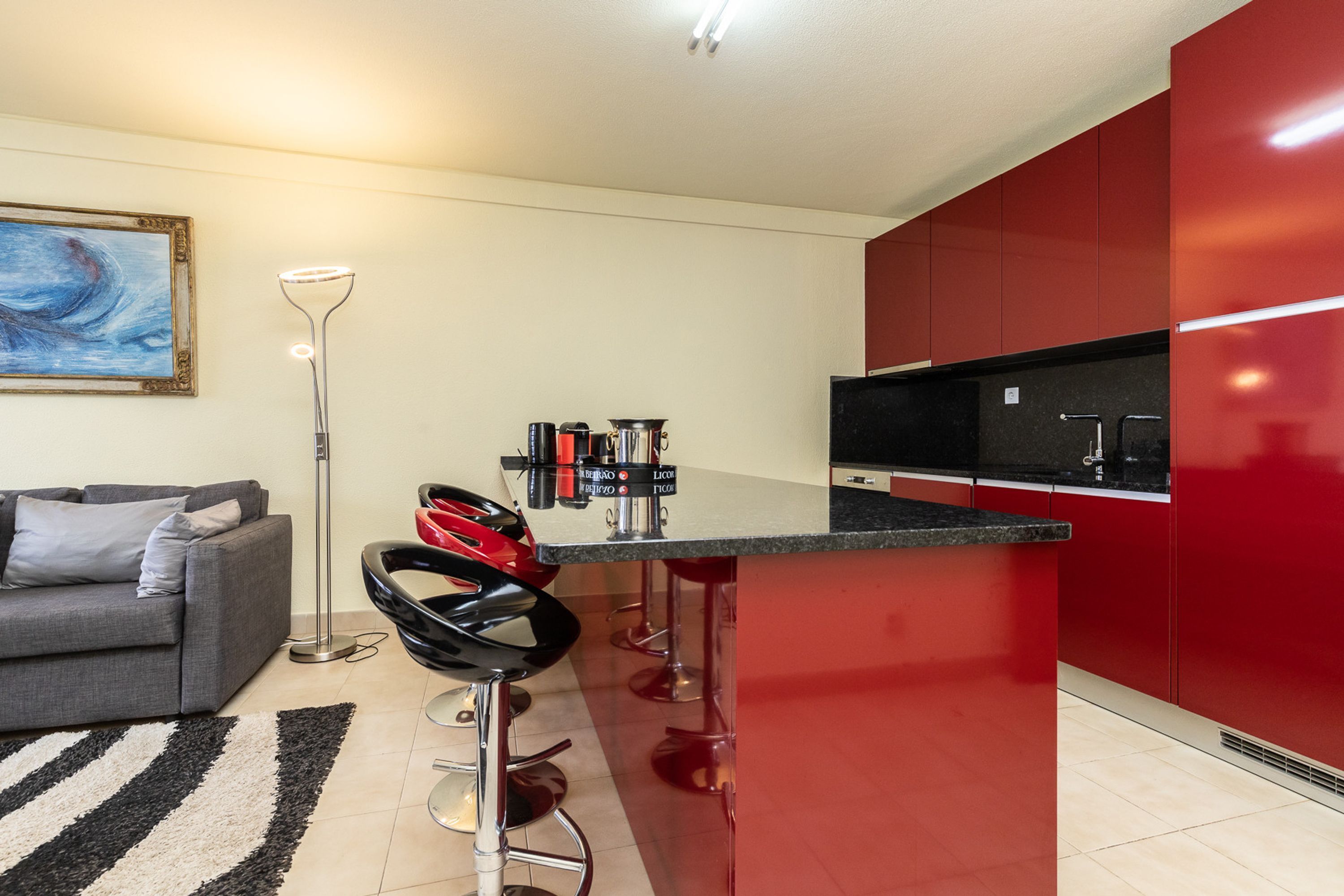 Una cucina moderna con mobili rossi, un piano di lavoro nero e un'area bar con sgabelli.