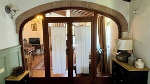 Un dormitorio con una cama grande, un aparador de madera, una mesita de noche y un escritorio con silla. Se ve un vanitorio que da a otra habitación con un televisor y una alfombra.