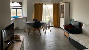 A modern living room with a dining area, a sofa, a TV, and a kitchen area with a window. - Alvor T1 1 Flat in Portim o (Portimão)
