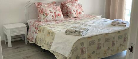 A bedroom with a bed, two bedside tables, a nightstand, a window with curtains, and a door.