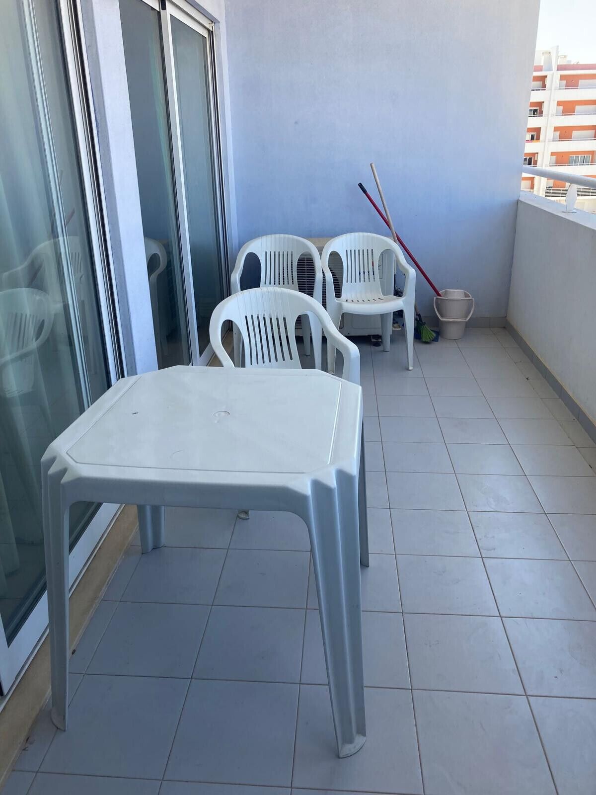 A balcony with a white plastic table and chairs, a broom, and a bucket.