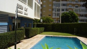 Una piscina rodeada por un seto bien cuidado, con un edificio que muestra la inscripción "RIVIERA DELAT" al fondo.