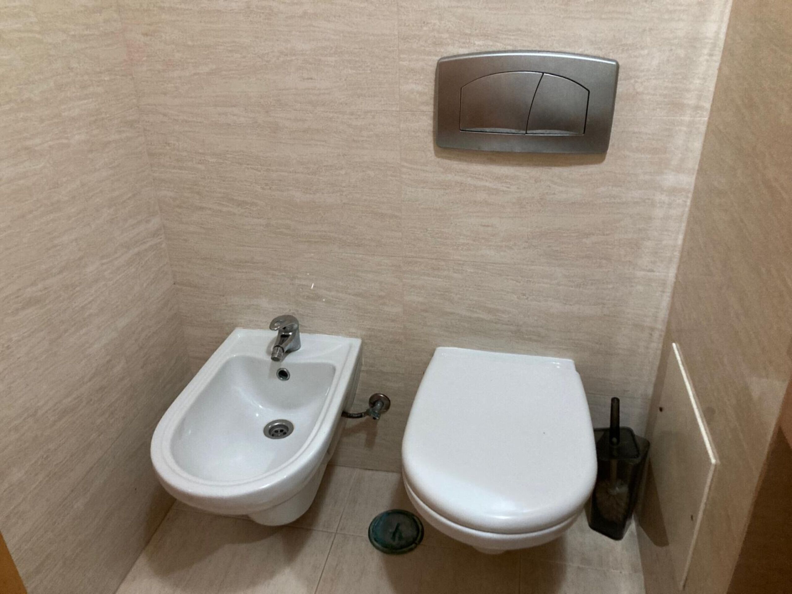Un baño pequeño con un bidé, inodoro y un accionador de descarga en la pared.