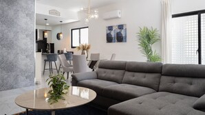 Moderni olohuone, jossa on kulmasohva, pyöreä sohvapöytä ja taustalla ruokailutila.