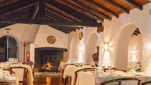 Ein Restaurant mit Holztischen und -stühlen, einem Kamin und Gewölbedecken.