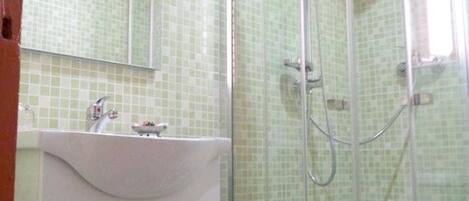 Un baño con ducha envuelta en vidrio, un lavabo y un espejo.