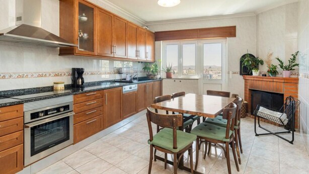 A modern kitchen with wooden cabinets, a granite countertop, a built-in oven, and a dining area with a table and chairs. - Douro 3 Bedrooms Magic Mountain Landscape (Vila Flor)