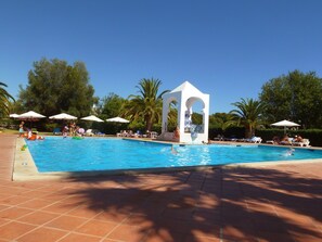 Una piscina con un pabellón blanco, palmeras y tumbonas.