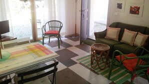 A room with a checkered floor, a green sofa with cushions, a wicker chair, a small round table, and a TV on a stand.