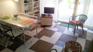 A room with a checkered floor, a desk with a computer, a chair, a wicker chair, and a bookshelf.