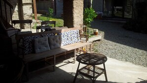 An outdoor seating area with a wooden bench and a metal table, surrounded by stone pillars and a gravel path.