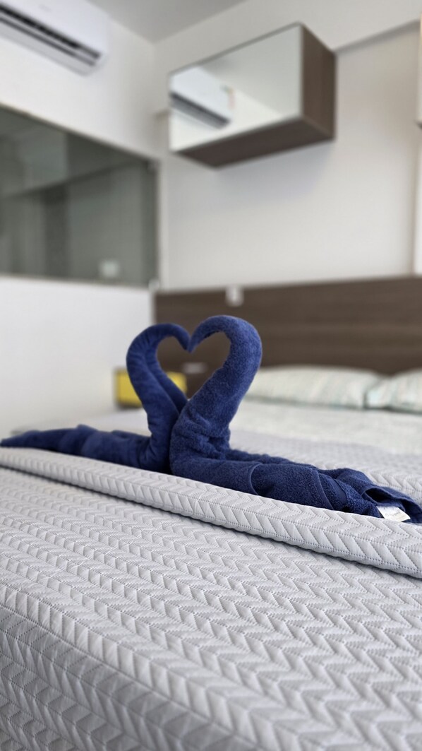 A bed with a white quilted bedspread and a blue towel arranged in a heart shape.