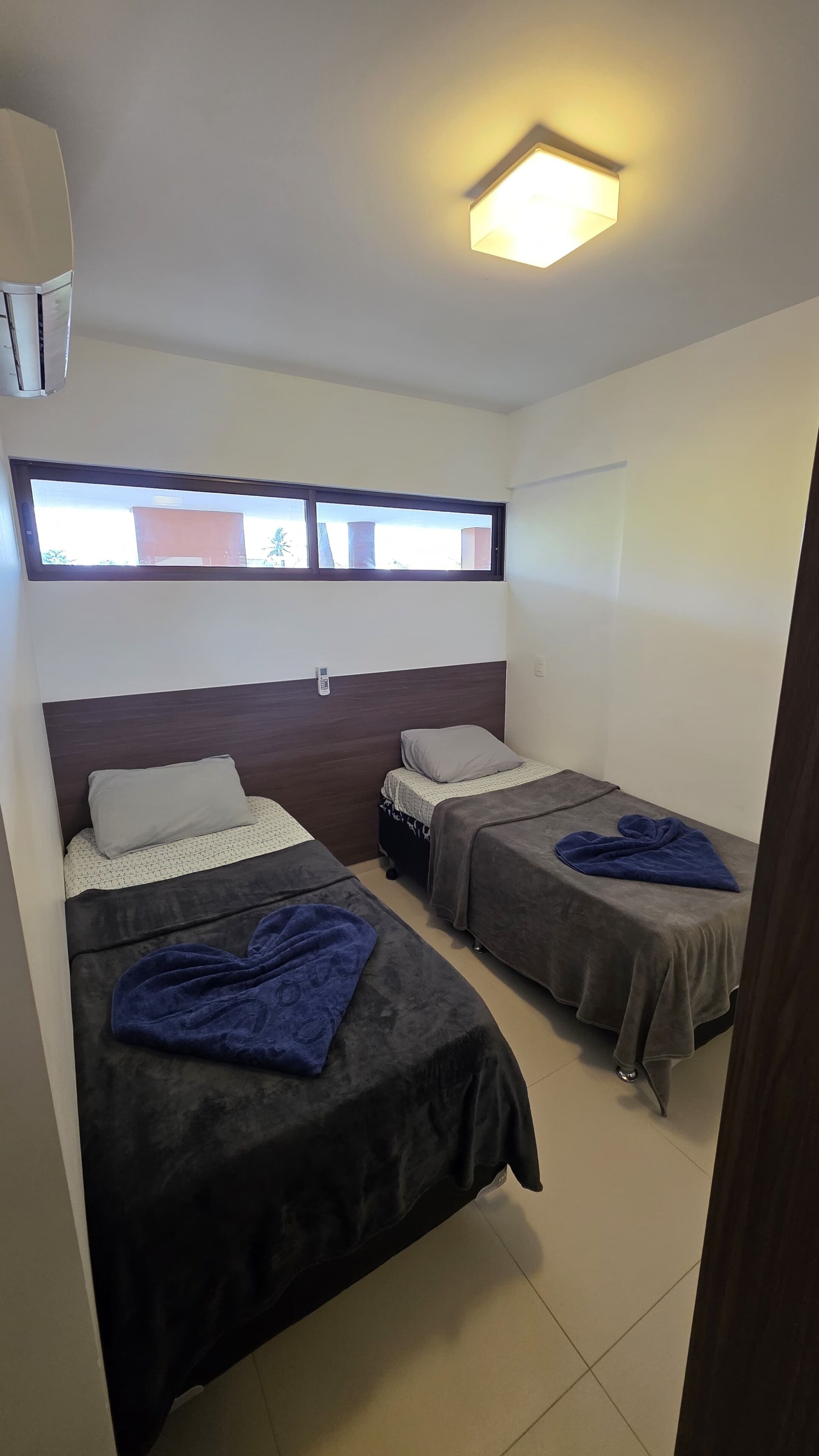 A room with two beds, a window, and a ceiling light.