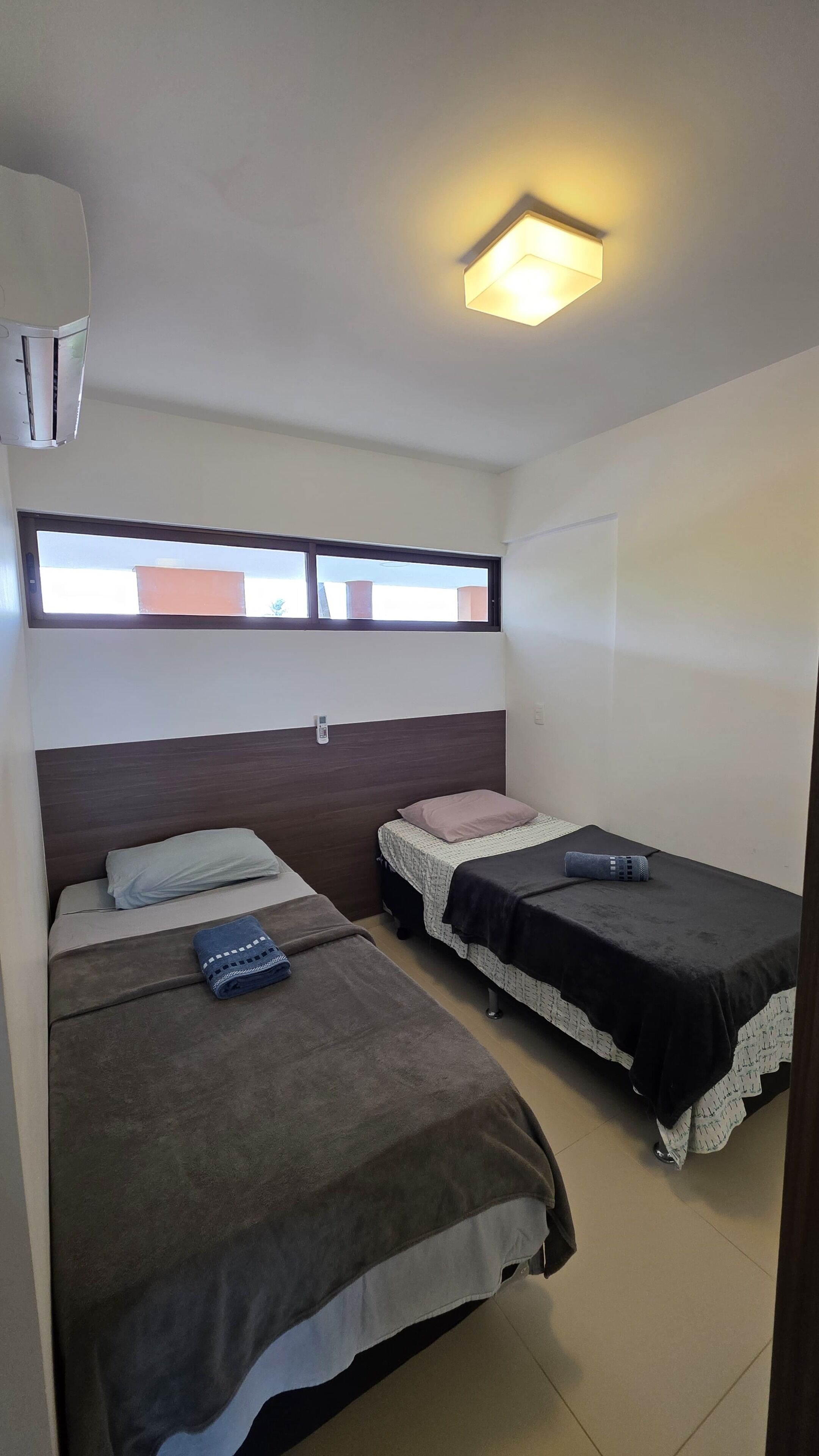 A room with two beds, a window, a ceiling light, and an air conditioning unit.