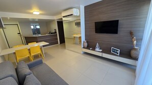 Moderni olohuone, jossa on sohva, ruokapöytä tuoleineen, keittiöalue ja seinälle asennettu litteänäyttöinen televisio. Seinä on tehty puusta.