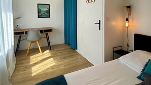 Et moderne soveværelse med en seng, et skrivebord og en stol. Der er en dør med lyskontakt og en vægmonteret lampe.
