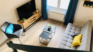 En moderne stue med et fladskærms-tv, en sofa, et sofabord og en lænestol.