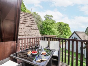 Un balcon avec une table en verre, des chaises en osier, une petite terrasse et une vue sur une maison et des arbres.