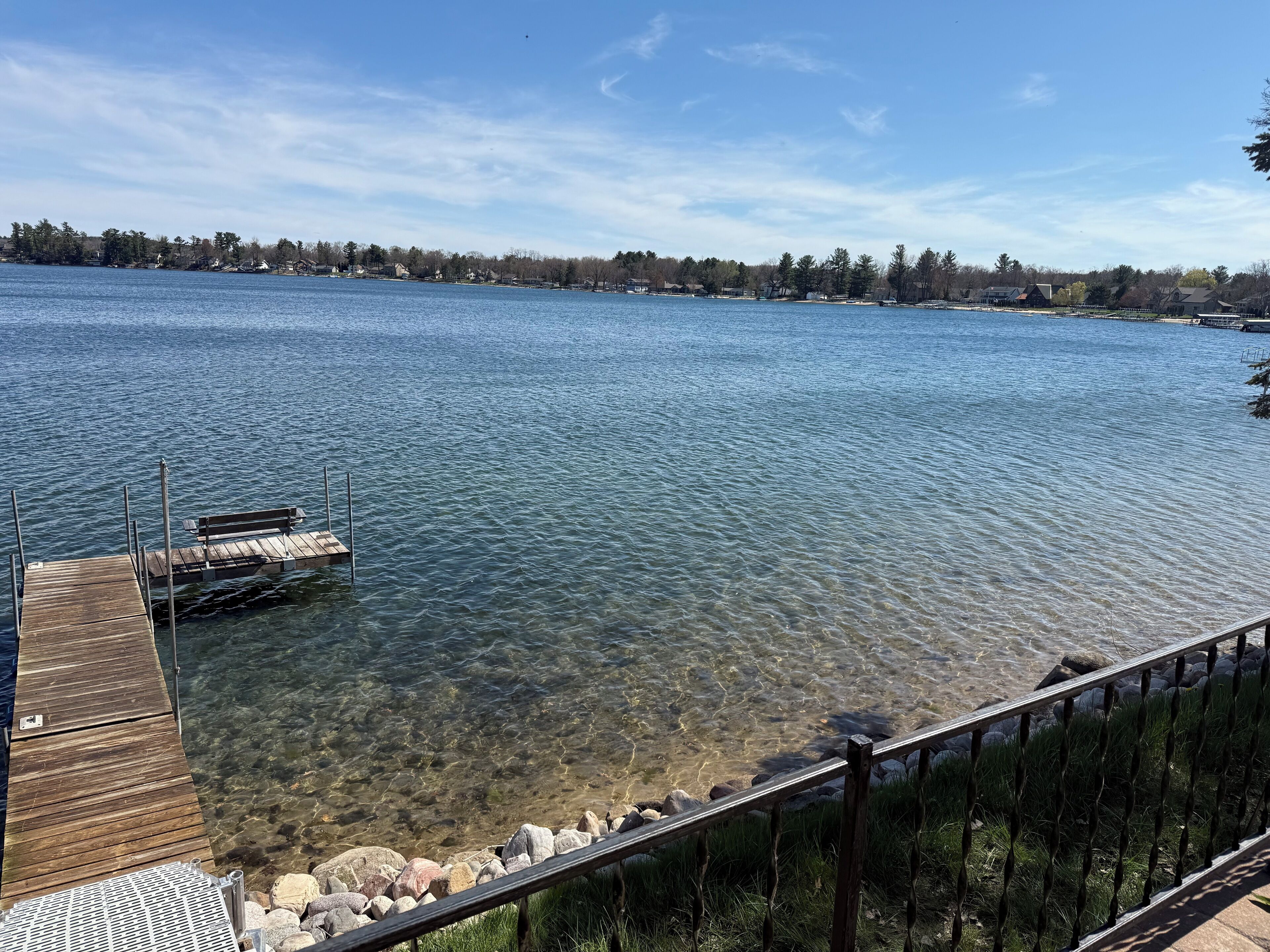 Vista despejada de un lago con un muelle de madera y barandilla metálica.