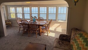 A dining area with a table and chairs, large windows with a view of the water, a lamp, and a sofa. - Retro Lakeside Charmer in Wonderful Wautoma with WiFi, AC and lake frontage (Wautoma)