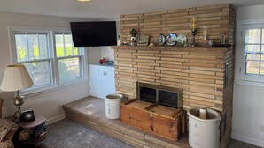 A living room with a brick fireplace, a television mounted above it, and a window with a view of the outdoors. - Retro Lakeside Charmer in Wonderful Wautoma with WiFi, AC and lake frontage (Wautoma)