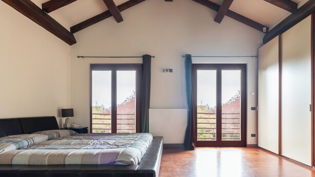 Een slaapkamer met een groot bed, houten vloer, nachtkastje en een raam met gordijnen.