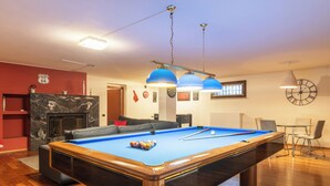 Een pooltafel in een kamer met een open haard, een klok en een eethoek.