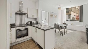 A modern kitchen with white cabinetry, a built-in oven, and a dining area with a table and chairs. - GuestReady - Urban getaway in Liverpool (Liverpool)