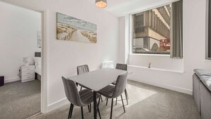 A modern dining area with a table and chairs, a painting on the wall, and a large window with a view of a building. - GuestReady - Urban getaway in Liverpool (Liverpool)