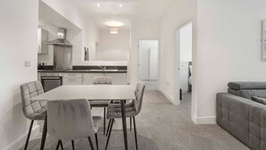 Una cucina moderna con isola centrale, un'area pranzo con tavolo e sedie, e un divano grigio in un soggiorno.
