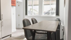 Habitación de hotel con una mesa de comedor, dos sillas, un cartel que dice "GUEST READY" y un ventanal con vistas a edificios.