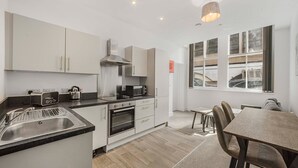 Una cocina moderna con armarios blancos, horno empotrado, microondas y tostadora. Hay una zona de comedor con mesa y sillas, y un ventanal con vistas a la ciudad.