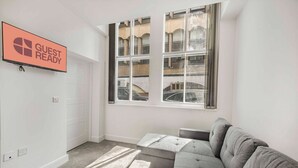 Una habitación moderna y minimalista con un sofá gris, una mesita pequeña y un televisor mostrando “GUEST READY”.