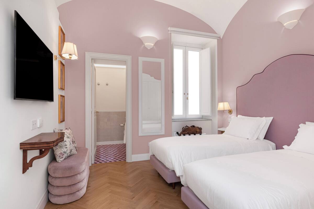 A bedroom with two beds, a television, a desk, and a bathroom door.