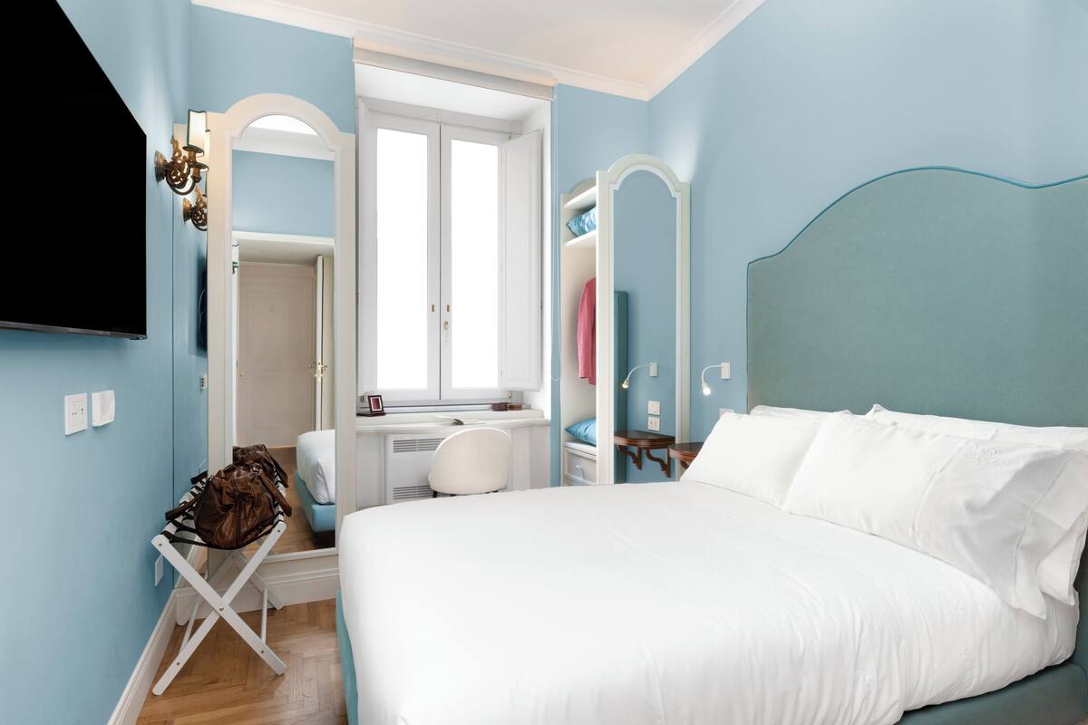 A bedroom with a bed, a desk, a chair, a mirror, and a wardrobe.