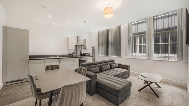 Un appartement moderne comprenant un coin repas, un ensemble de canapés et une cuisine équipée d’un four et d’un micro-ondes intégrés.
