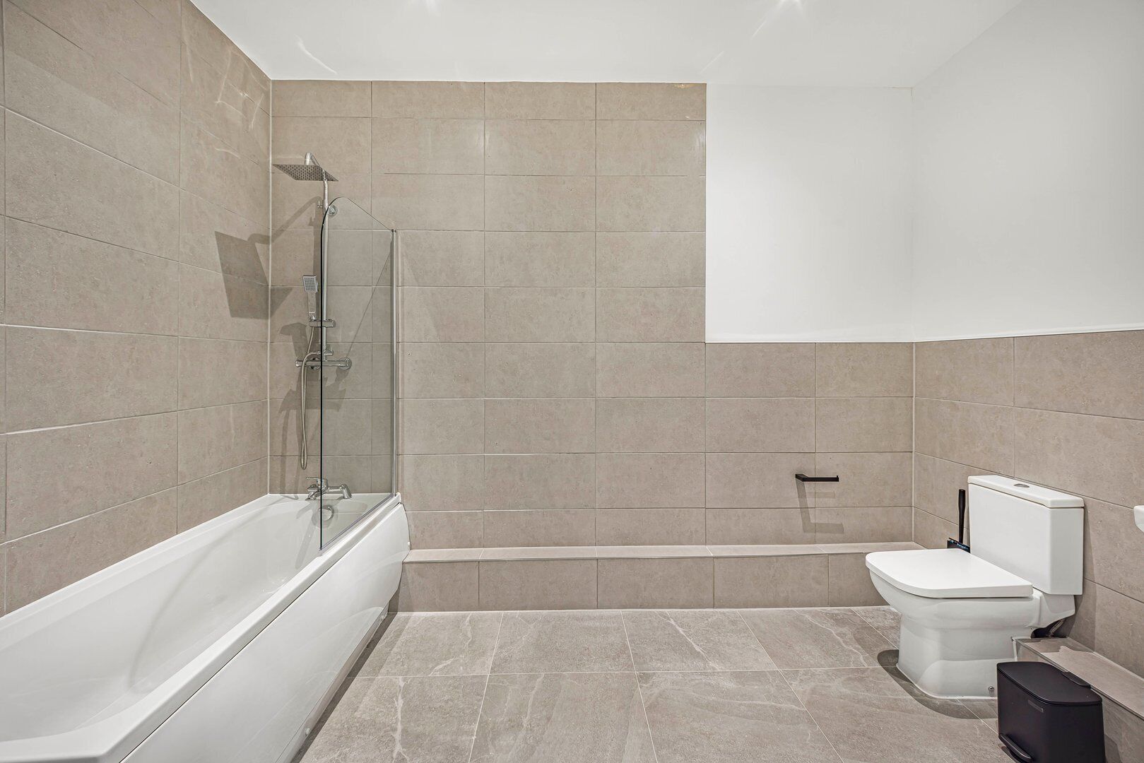 A modern bathroom with a glass-enclosed shower, a white bathtub, and a toilet.