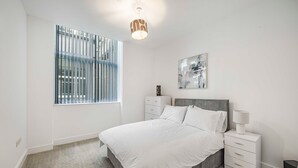 A bedroom with a bed, a nightstand, a lamp, a speaker, and a window with blinds. - GuestReady – Relaxing retreat in Liverpool (Liverpool)