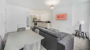 A modern, well-lit room with a dining table, grey upholstered sofa, and a kitchen area. - GuestReady – Relaxing retreat in Liverpool (Liverpool)
