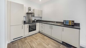 A modern kitchen with white cabinets, a stainless steel range hood, a built-in oven, a microwave, and a sink. - GuestReady – Relaxing retreat in Liverpool (Liverpool)