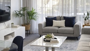 A modern living room with a sofa, coffee table, and TV. - Walk to Elizabeth Quay | Pool & Parking (Perth)