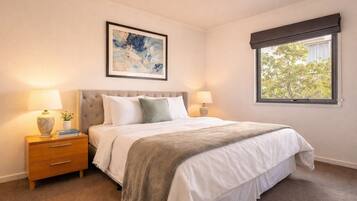A bedroom with a bed, bedside tables, a window with a view, and a painting on the wall.