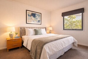 A bedroom with a bed, bedside tables, a window with a view, and a painting on the wall.