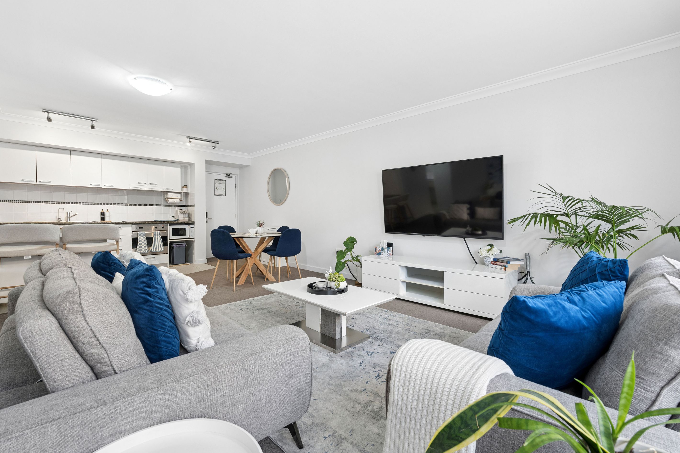 A modern living room with a grey sofa, a coffee table, and a flat-screen TV mounted on the wall.