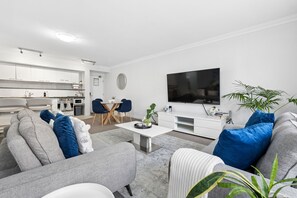 A modern living room with a grey sofa, a coffee table, and a flat-screen TV mounted on the wall. - Tulizo  | Walk to Elizabeth Quay • Pool & Parking (Perth)