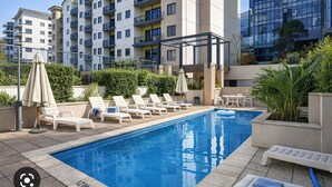 A swimming pool with lounge chairs and umbrellas, surrounded by apartment buildings. - Walk to Elizabeth Quay | Pool & Parking (Perth)
