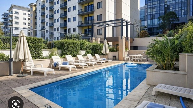 A swimming pool with lounge chairs and umbrellas, surrounded by apartment buildings. - Tulizo  | Walk to Elizabeth Quay • Pool & Parking (Perth)